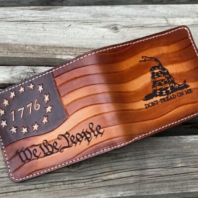 “Hand-tooled ‘We The People’ 1776 Gadsden Flag leather bifold wallet. Premium full-grain leather with Betsy Ross stars, Don’t Tread On Me rattlesnake, and bold patriotic design. Handcrafted in the USA. Perfect patriotic gift for men.”