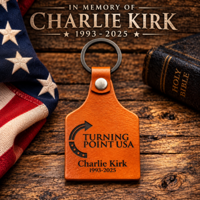 Charlie Kirk memorial leather keychain featuring the Turning Point USA logo and 1993-2025 dates, displayed on rustic wood with an American flag and bible tribute background
