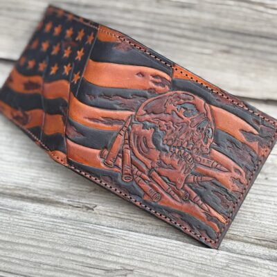 Hand-tooled leather bifold wallet featuring a distressed American flag with battle-worn skull and bullets. Premium full-grain leather, patriotic tactical design. Perfect veteran & 2nd Amendment gift.